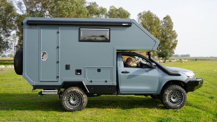 a truck with a camper attached to it's bed in the grass near some trees