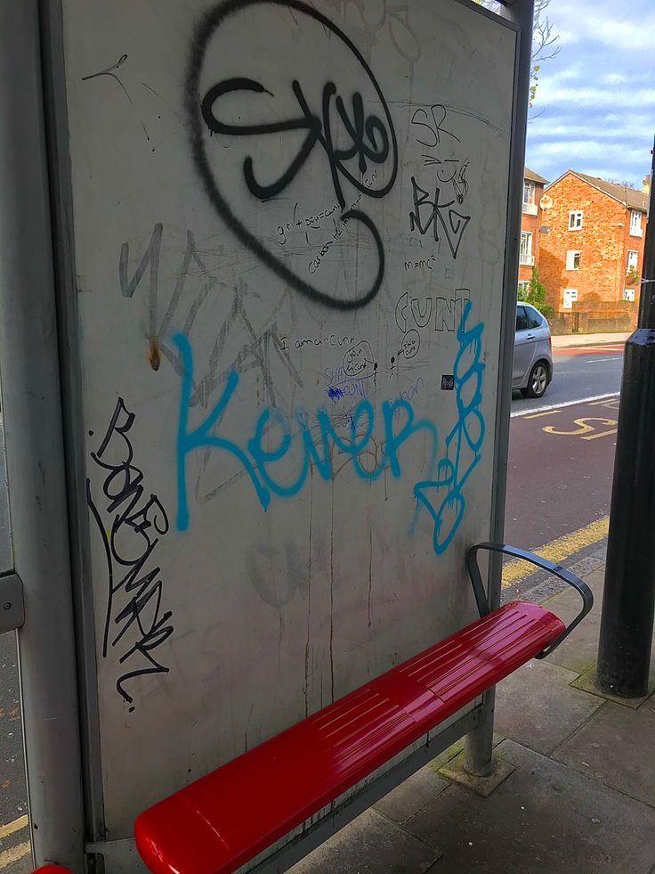 a red bench sitting on the side of a road next to a wall covered in graffiti