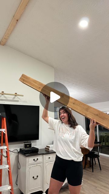 a woman holding up a large piece of wood in her hand while standing next to a ladder