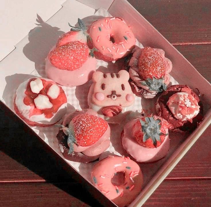 a box filled with donuts covered in frosting and strawberries on top of a wooden table