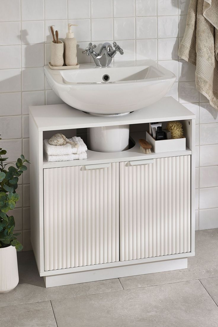 a white sink sitting on top of a wooden cabinet next to a potted plant