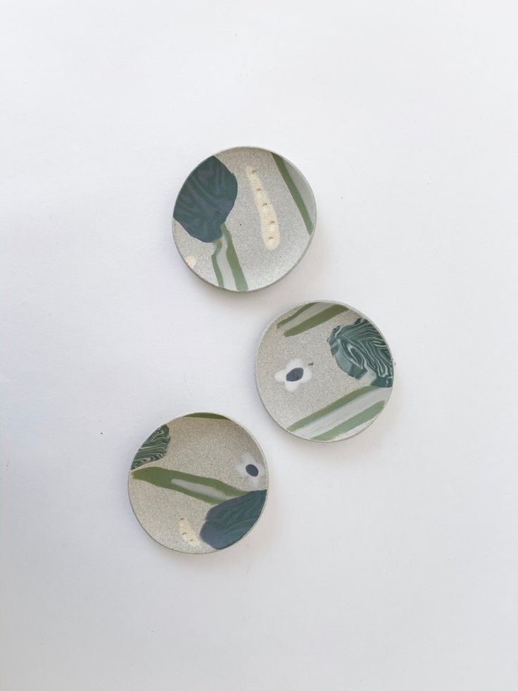 three ceramic buttons sitting on top of a white surface with green leaves and flowers painted on them