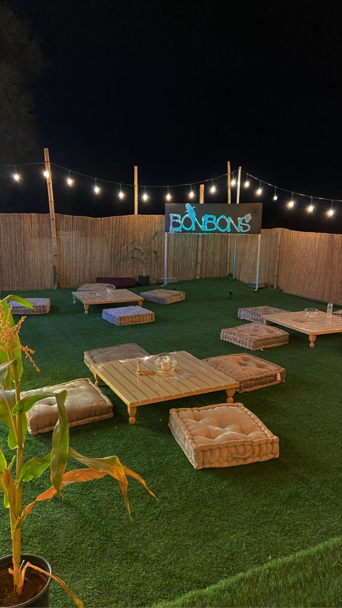 an outdoor seating area is lit up at night with string lights strung across the fence