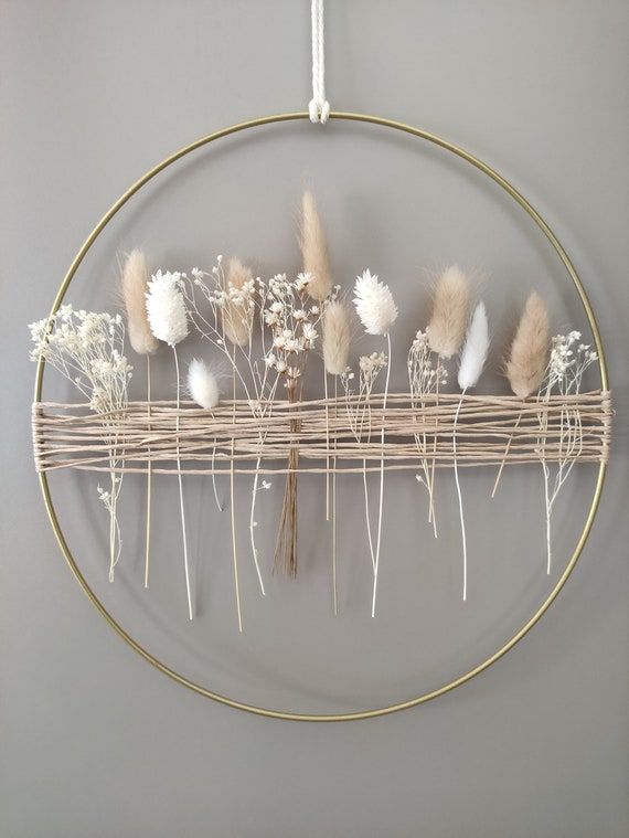 a circular metal rack with dried flowers on it hanging from the wall in front of a gray wall