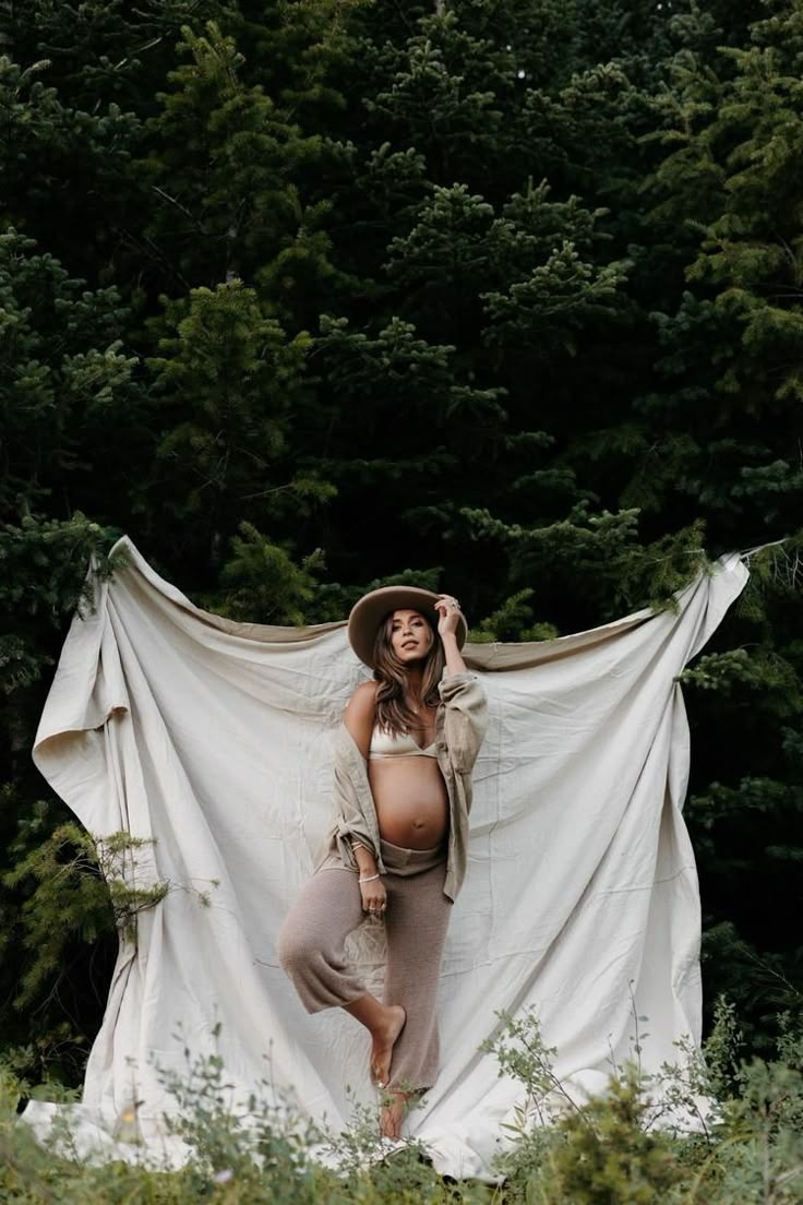 a pregnant woman standing in front of trees with a white sheet draped over her head