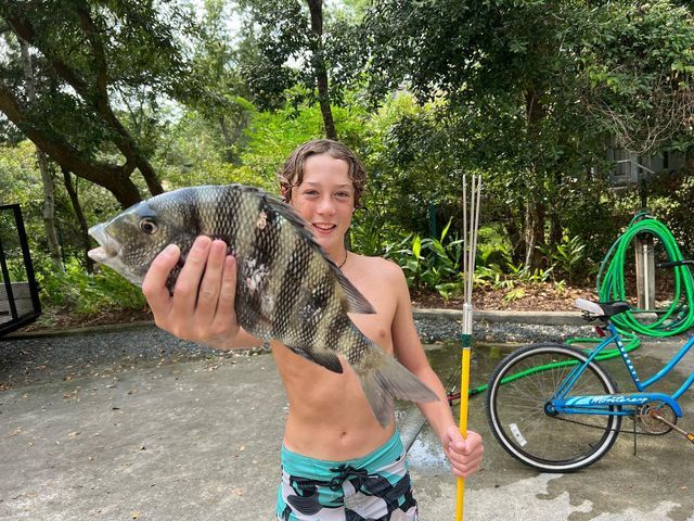 a young boy holding up a fish in front of a bike and bicycle racket