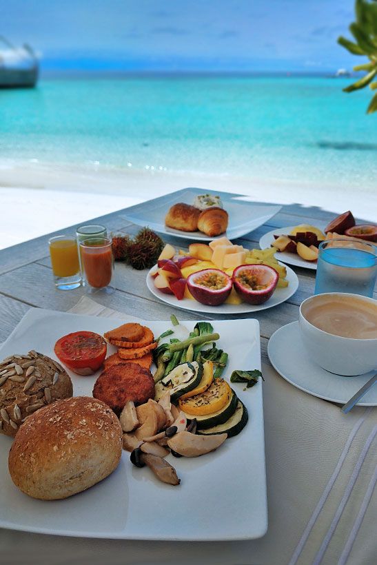 a table topped with plates of food next to an ocean side covered in fruit and veggies