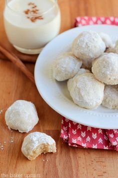 a white plate topped with snowball cookies next to a glass of milk and cinnamon sticks