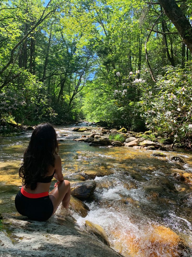 a woman sitting on top of a rock next to a river filled with water and trees