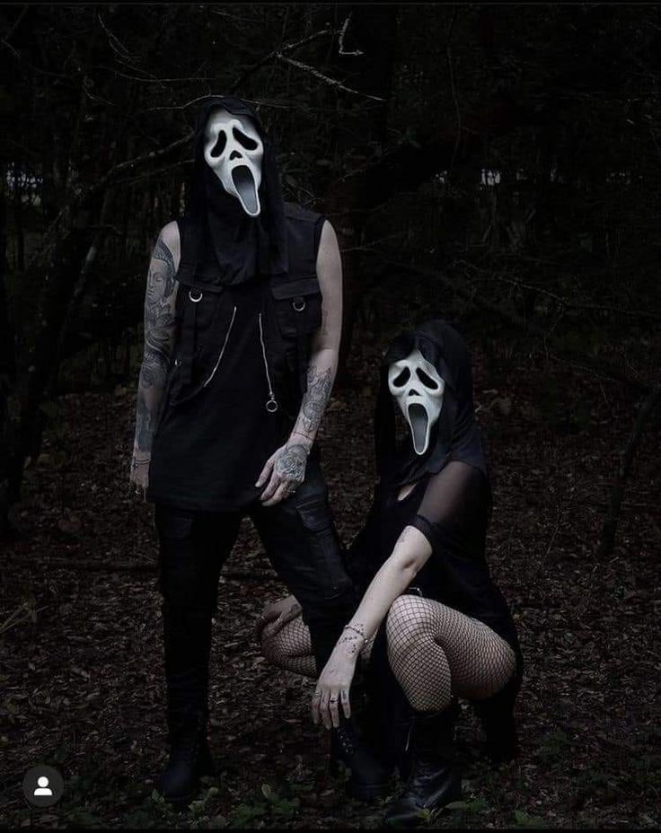 two people with masks on their faces in the woods at night, one is wearing a mask and the other wears a black outfit