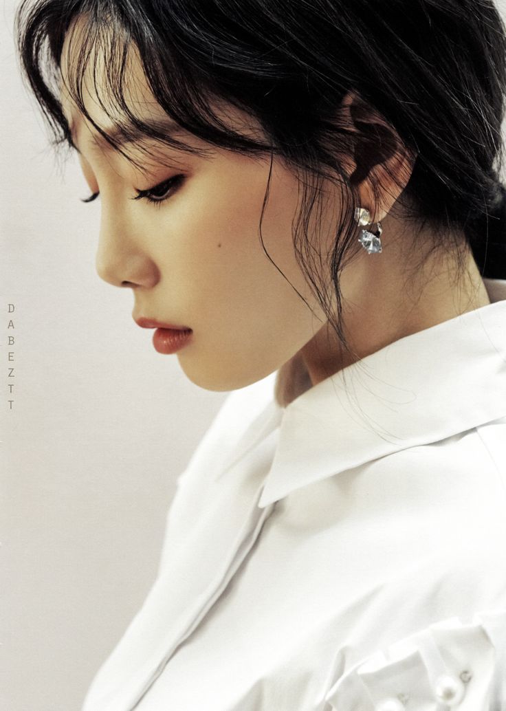 a woman with black hair and earrings on her head looking off to the side while wearing a white shirt