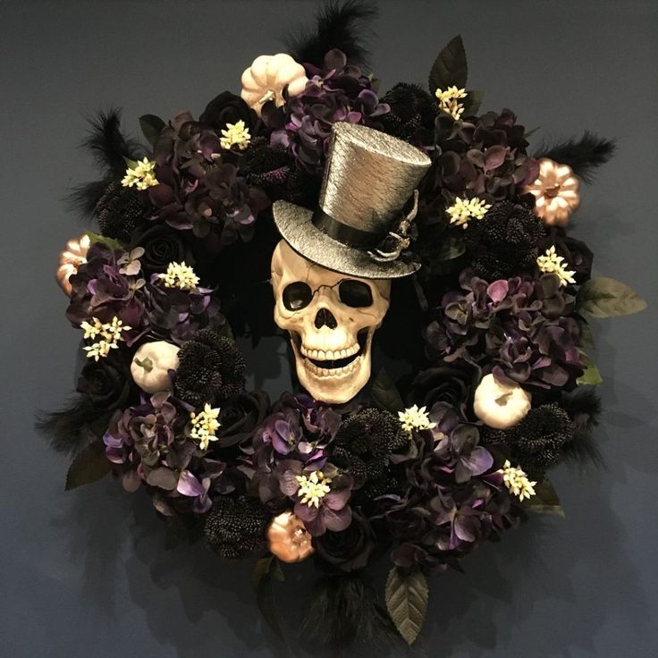 a skeleton wearing a top hat with flowers and feathers on it's head in front of a wreath