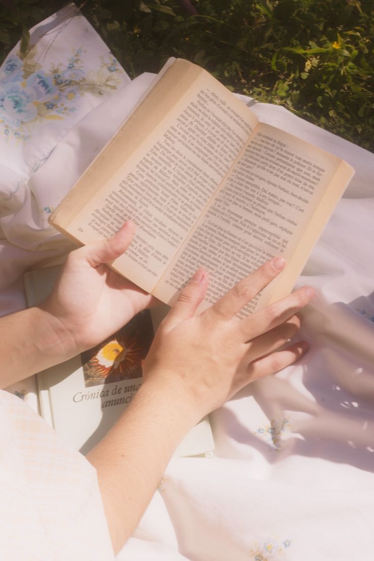 a person laying on top of a bed holding an open book in front of them