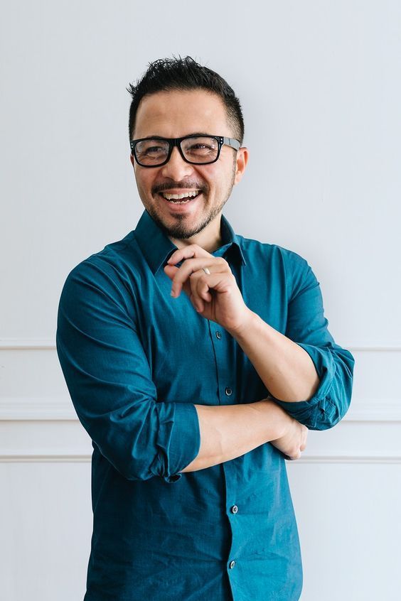 a man with glasses is smiling and looking at the camera while standing in front of a white wall