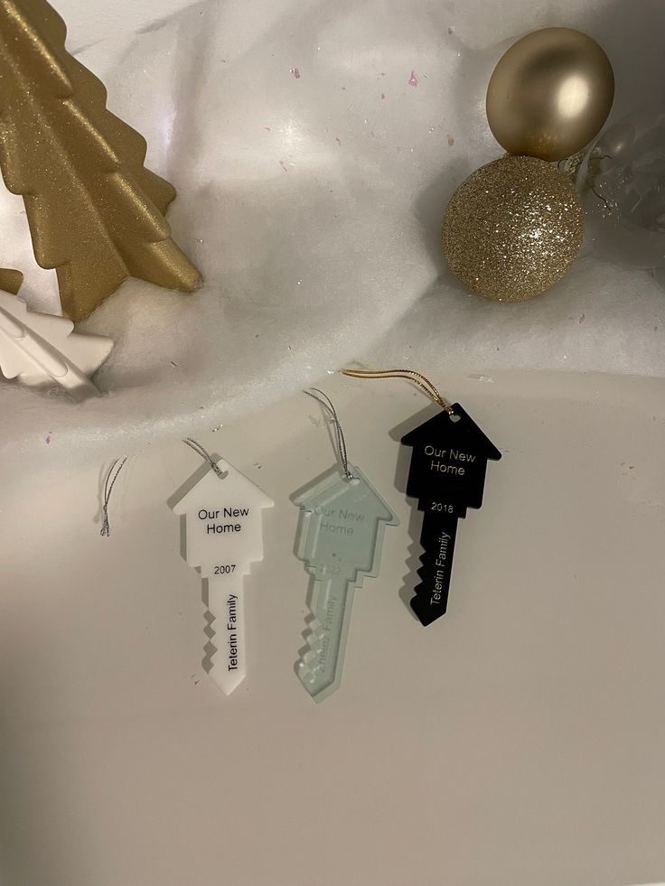 three key shaped ornaments sitting on top of a white surface next to a gold christmas tree