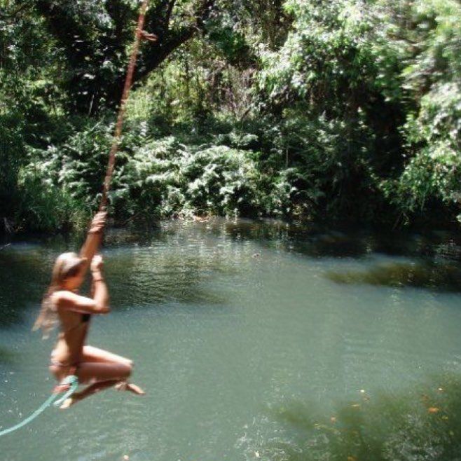 a woman is hanging from a rope in the water while holding onto a tree branch