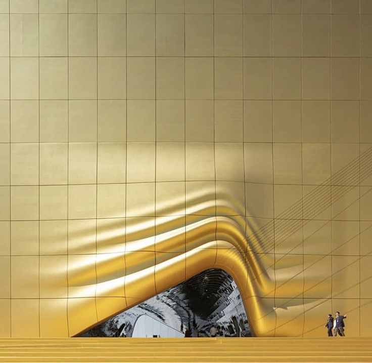 two people are standing in front of a yellow wall with an abstract design on it