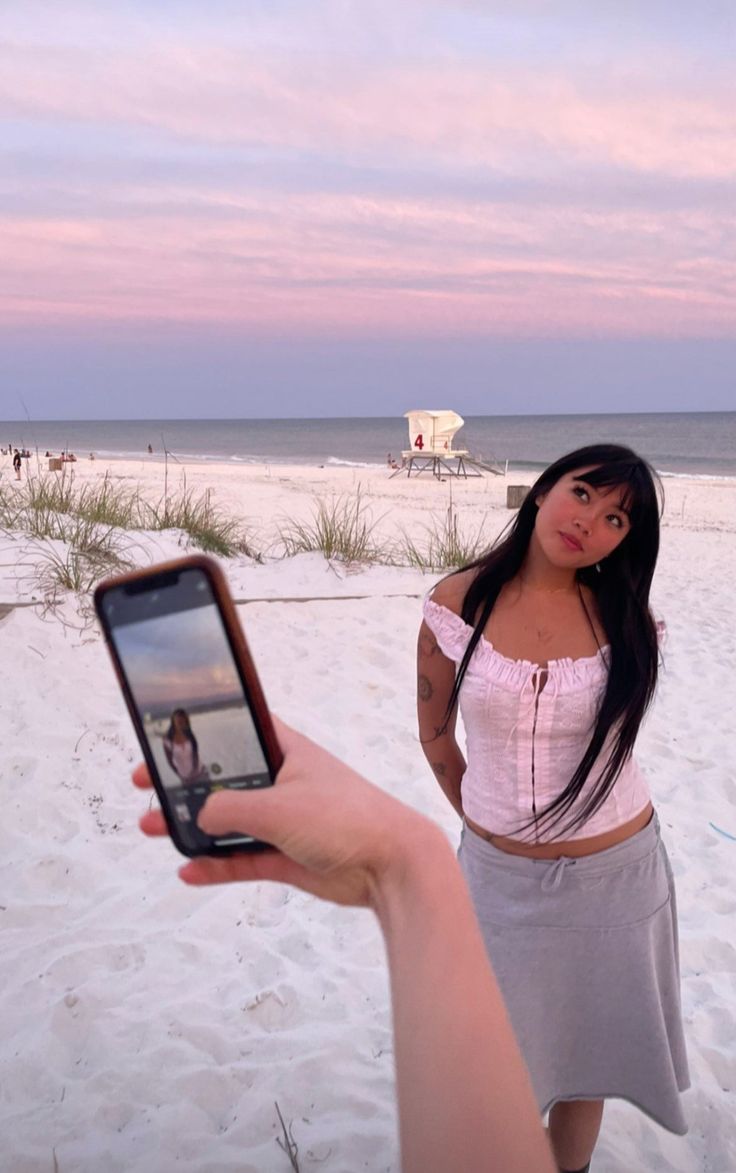 a woman holding up a cell phone to take a photo on the beach at sunset