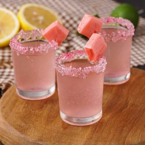 three glasses filled with watermelon margaritas on top of a wooden cutting board