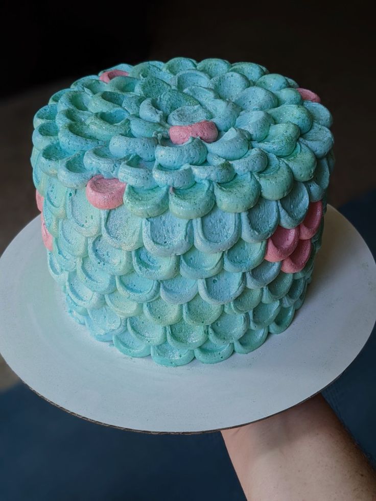 a blue cake with pink and green icing on a white plate being held by someone's hand