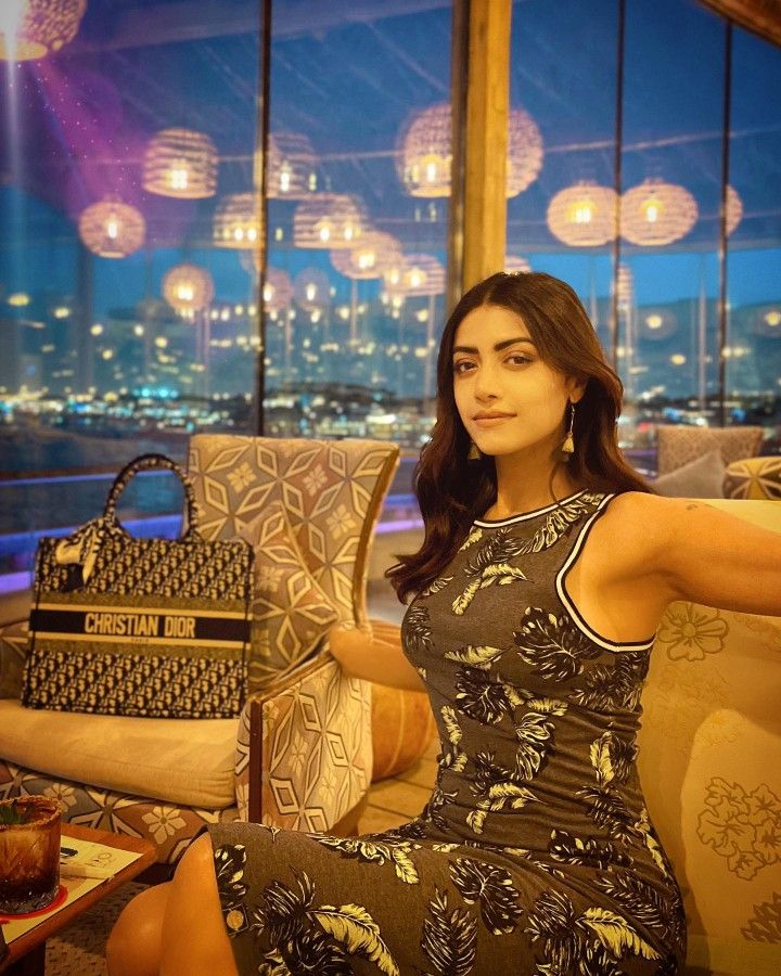 a woman sitting on top of a couch in front of a window with lights hanging from the ceiling