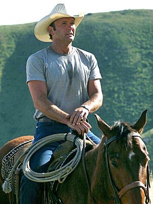 a man riding on the back of a brown horse next to a lush green hillside