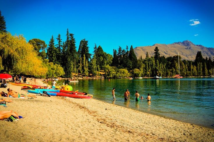 many people are on the beach with canoes and kayaks in the water near some trees