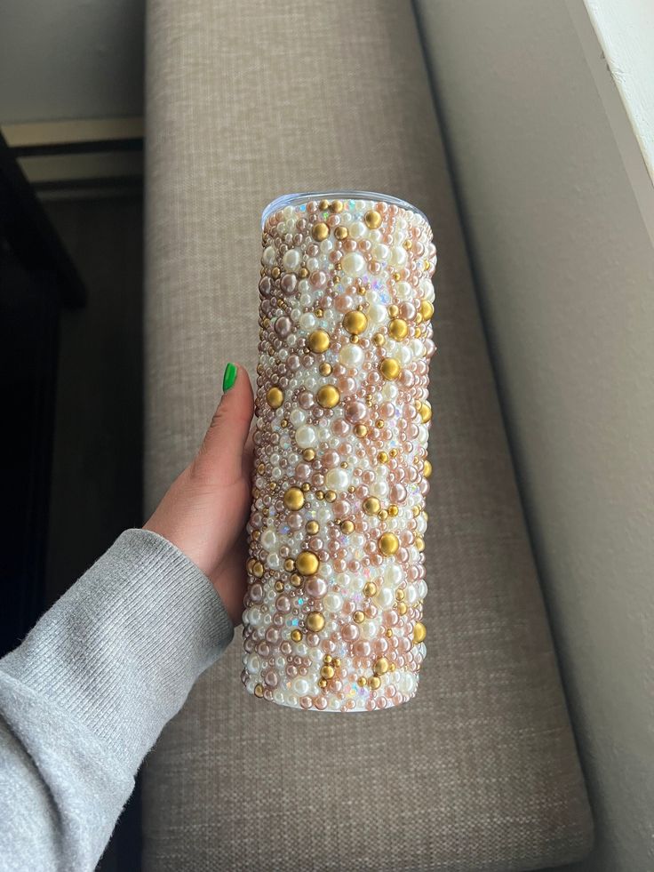 a hand holding a cup that is covered in pearls and gold flecks on a couch