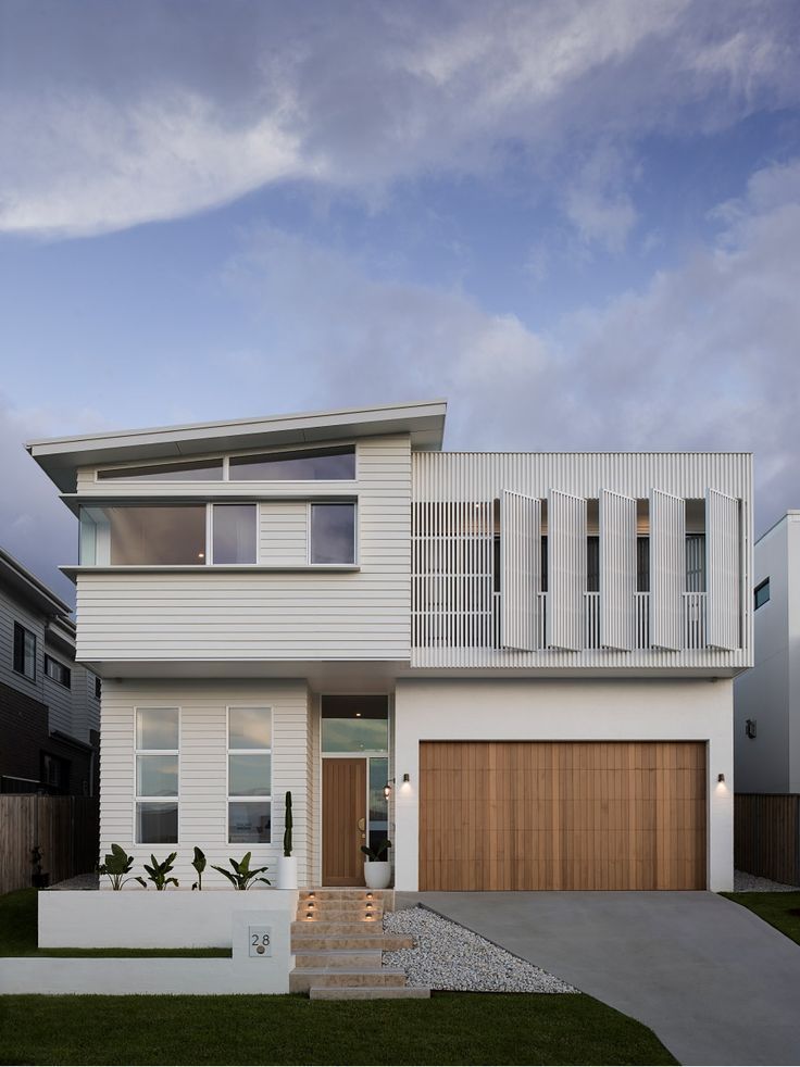 a modern house with white siding and wood accents on the front door is shown at dusk