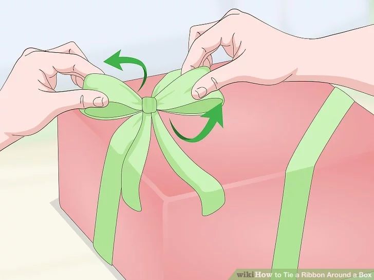 a person tying a green ribbon around a pink gift box