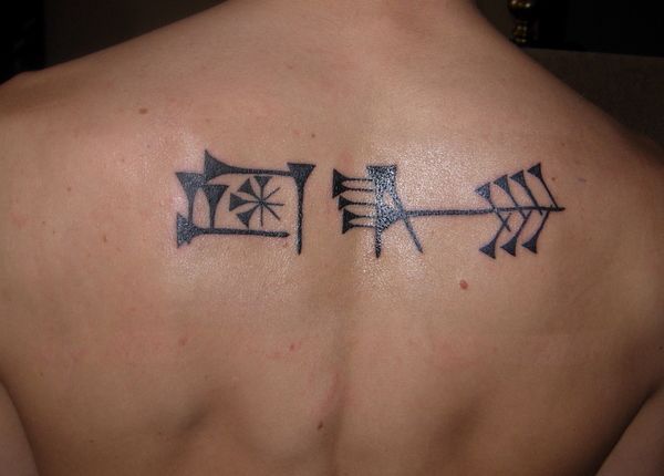 the back of a man's shoulder with an arrow and cross tattoo on it