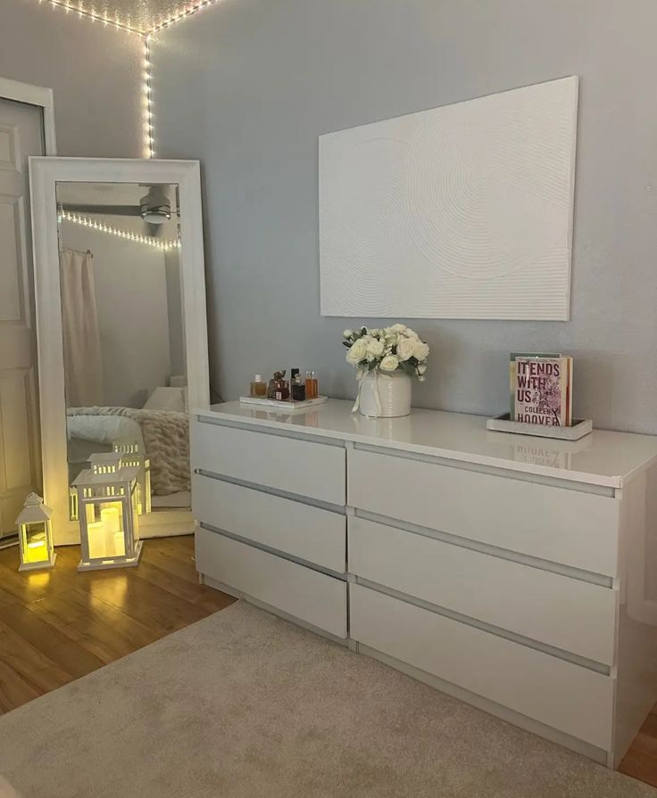 a white dresser sitting in a bedroom next to a bed with lights on top of it