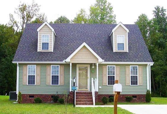 a gray house with two windows and a front porch in the middle of a grassy area