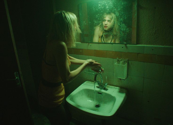 a woman standing in front of a bathroom sink under a mirror with green light shining on her