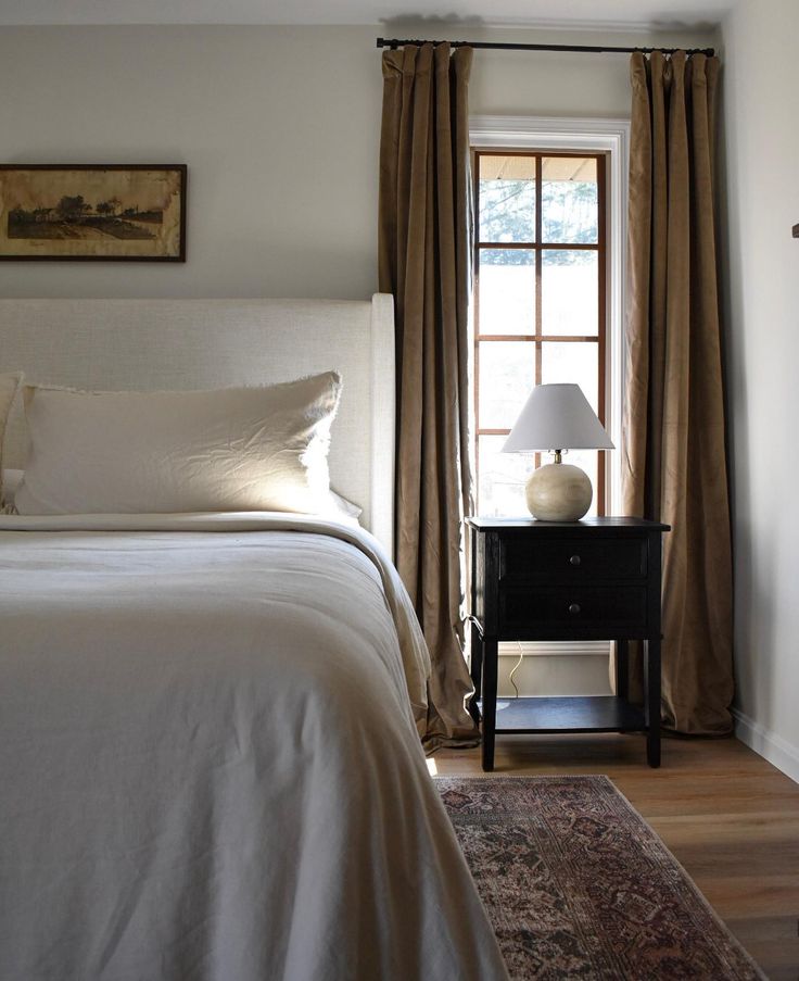 a white bed sitting next to a window in a bedroom on top of a wooden floor