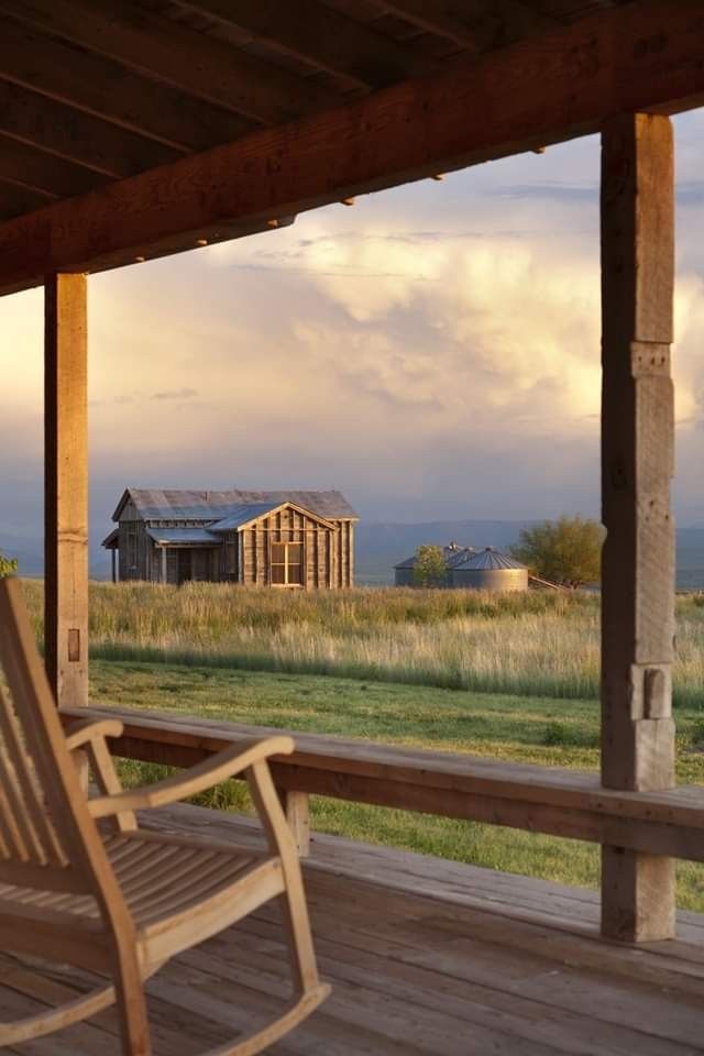 a wooden rocking chair sitting on top of a wooden deck next to a building with a barn in the background