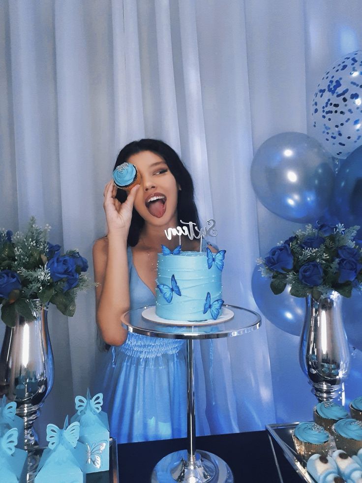 a woman holding a cupcake in front of her face while standing next to a cake