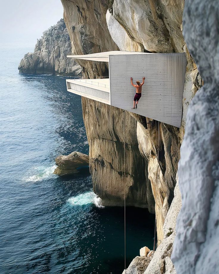 a man hanging off the side of a cliff next to the ocean