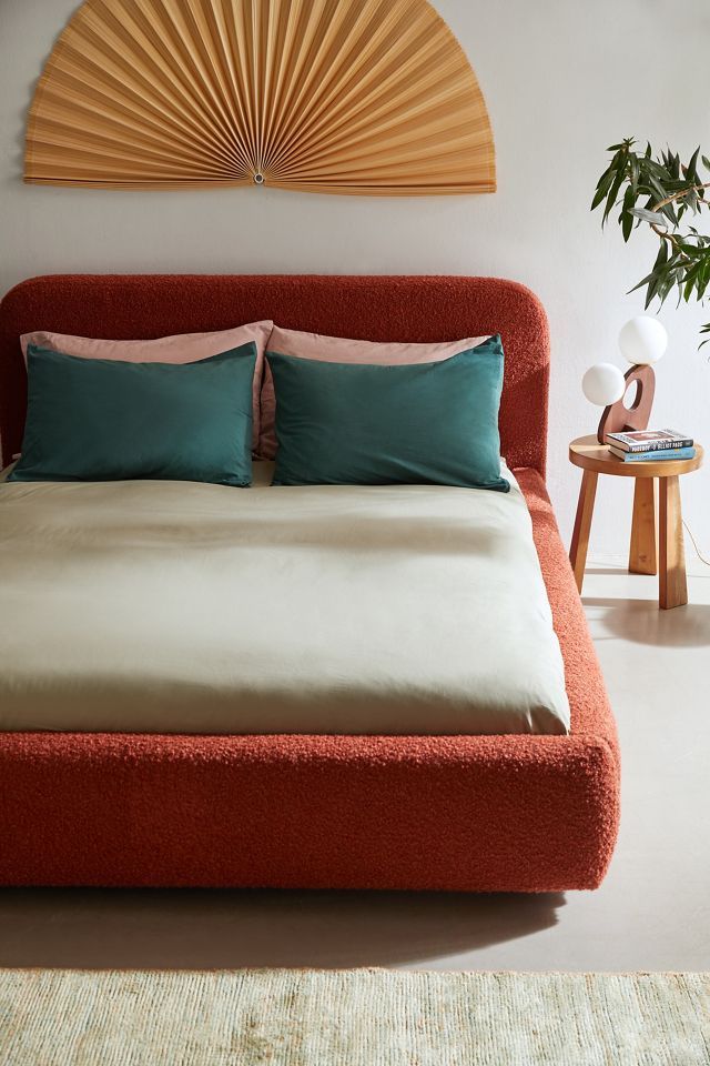 a bed with two pillows on top of it next to a table and potted plant