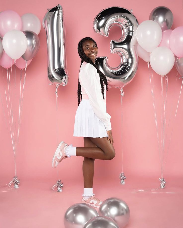 a young woman poses in front of balloons and the number twenty five, with her legs crossed