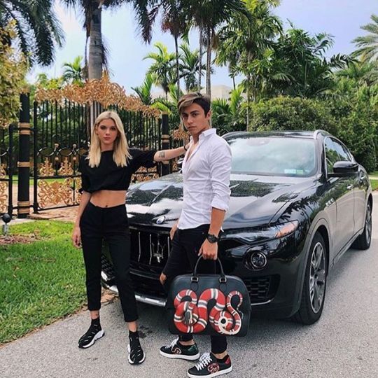 a man and woman standing next to a black car in front of some palm trees