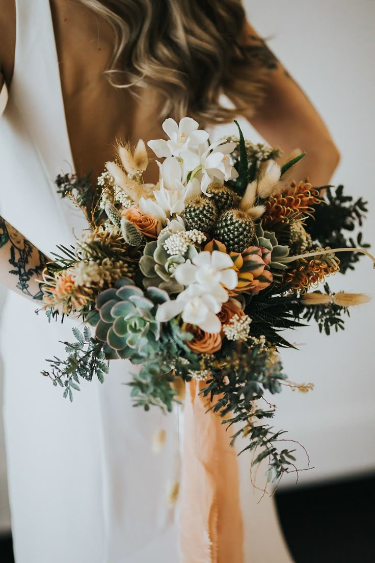 a woman holding a bouquet of flowers in her hands and wearing a white dress with an orange sash