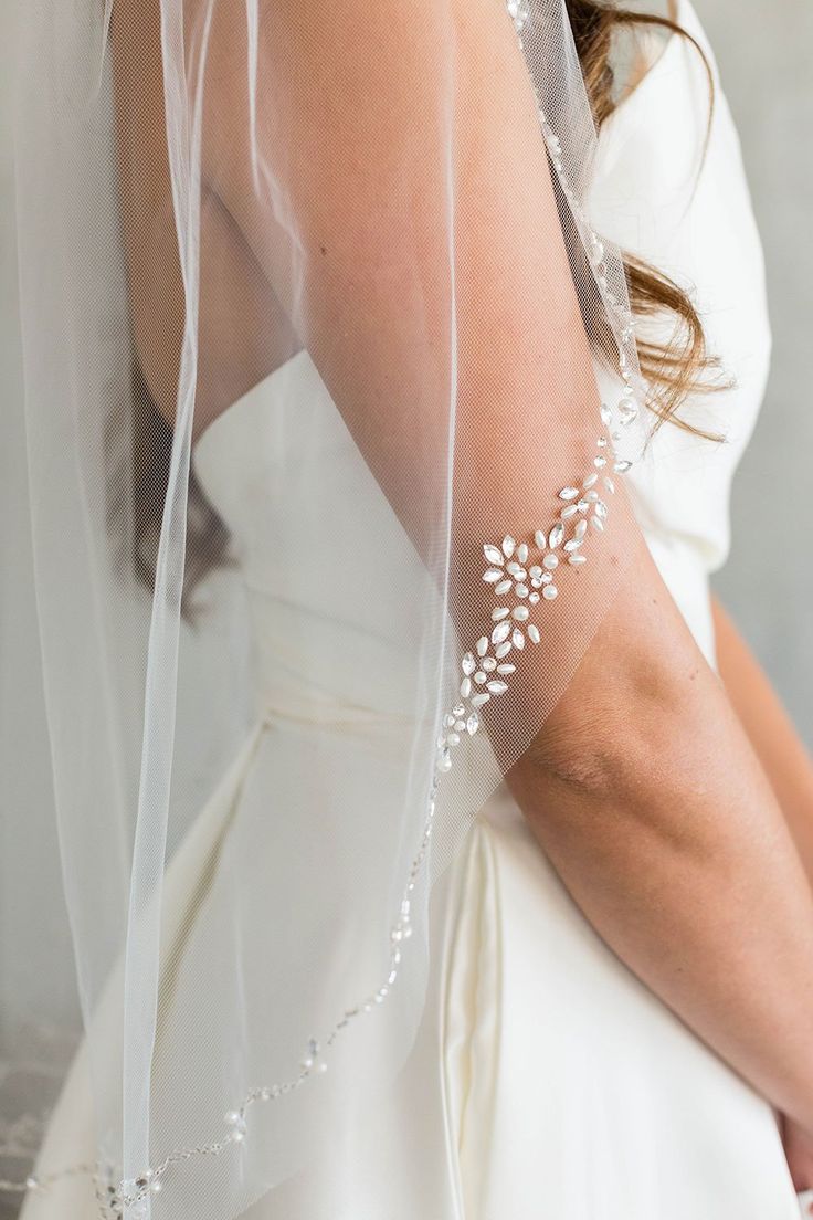 a woman in a wedding dress with a veil on her head and flowers on her arm