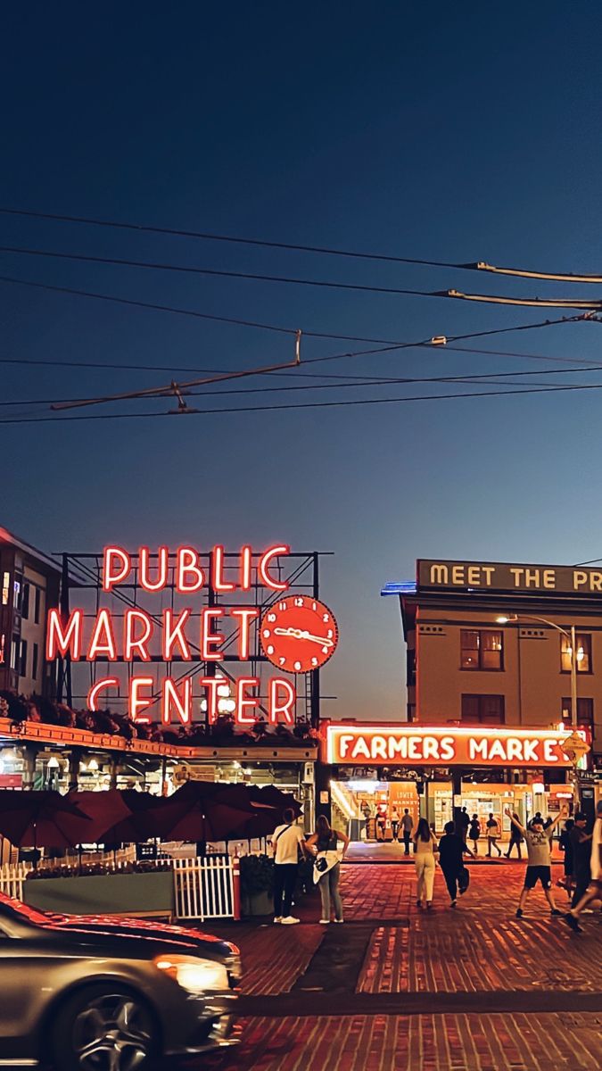 people are walking on the sidewalk in front of a market and some buildings at night