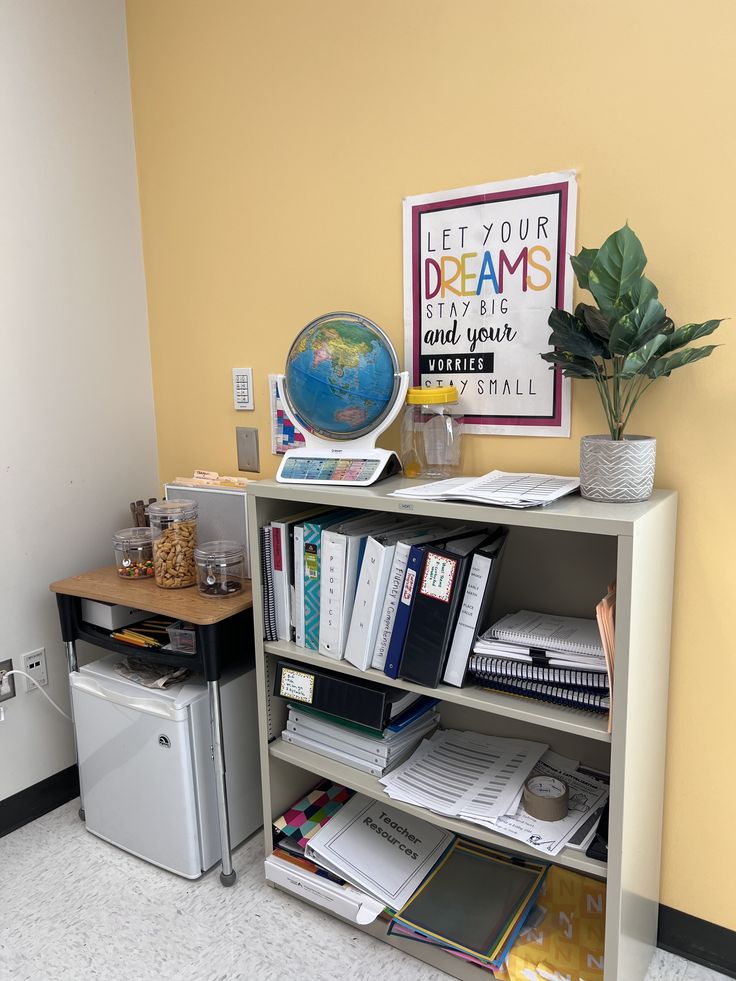 a book shelf filled with books next to a refrigerator and a globe on the wall