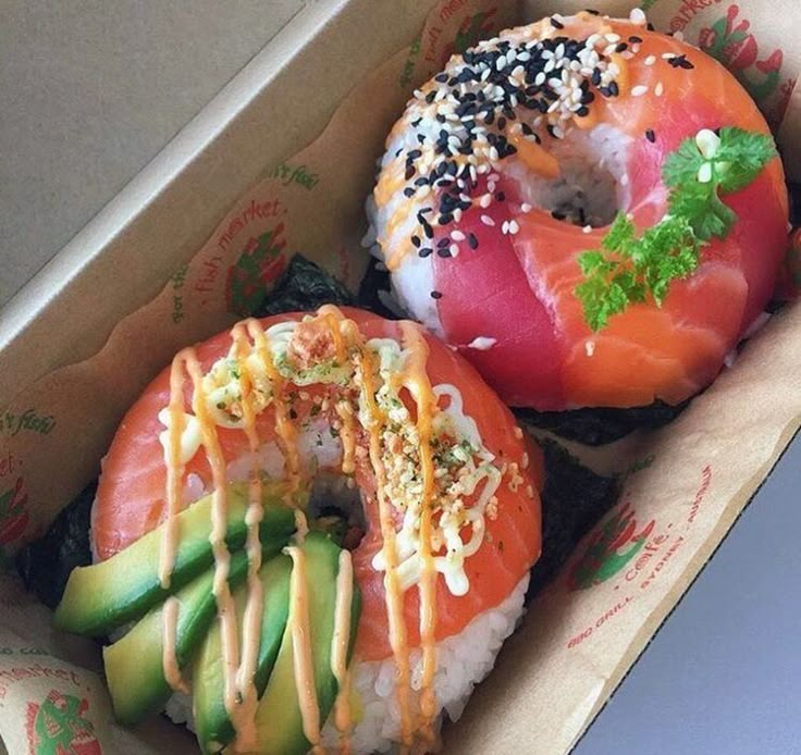 two sushi donuts in a box with toppings on the top and bottom