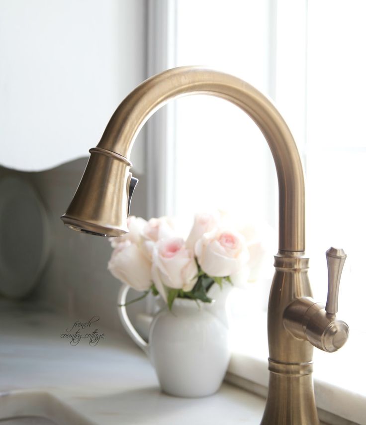 a white vase with pink roses in it next to a faucet on a window sill