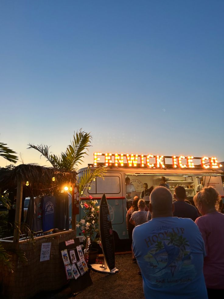 a group of people standing in front of a food truck at night with lights on