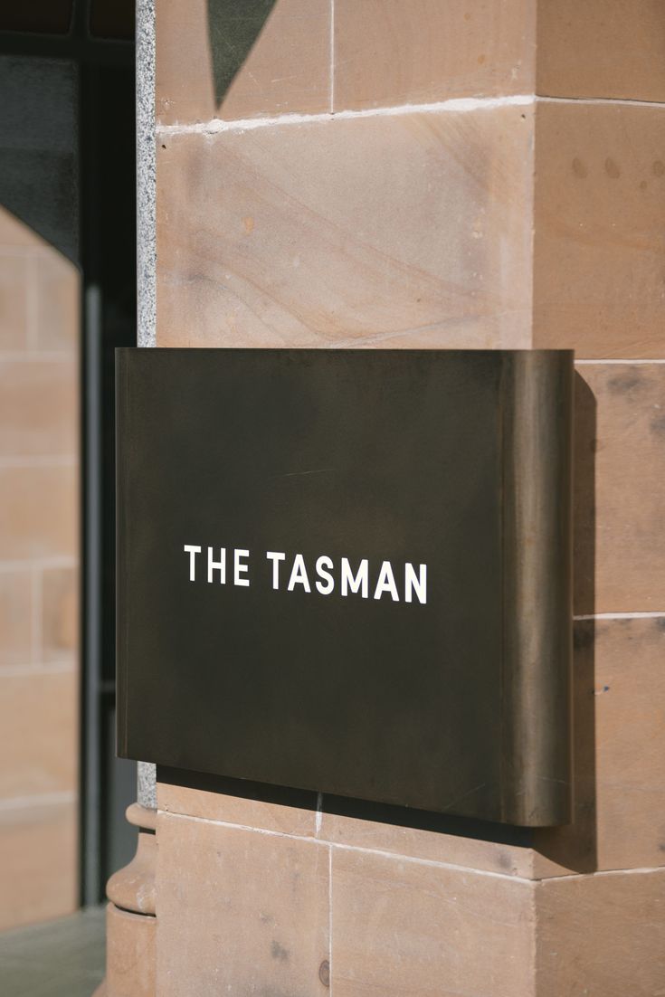 there is a sign that says the tasman on it's outside wall and in front of a brick building