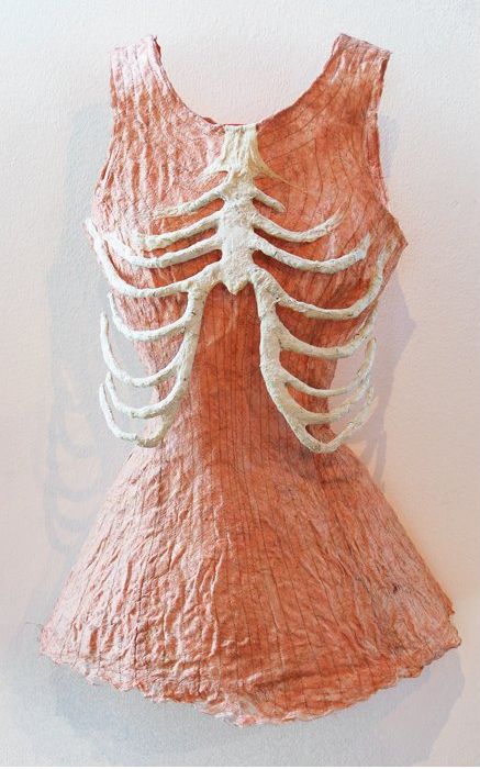 an orange dress with white strings attached to the chest and back, hanging on a wall